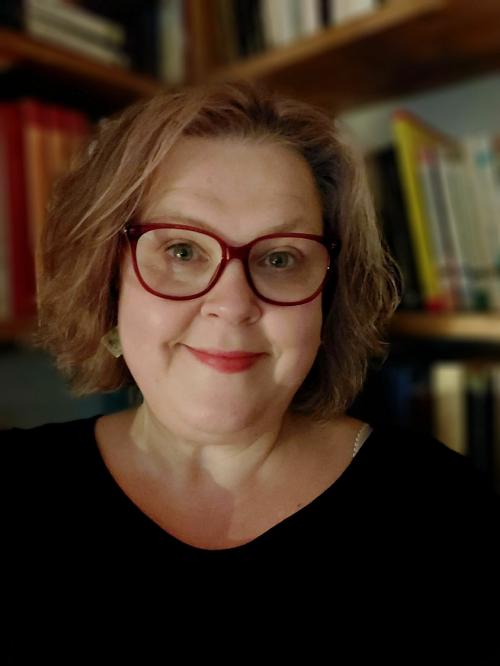 Headshot of Professor Hooper wearing black and standing in front of a bookcase like a proper academic