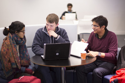Image of a group of students in discussion, sat at a table with laptops